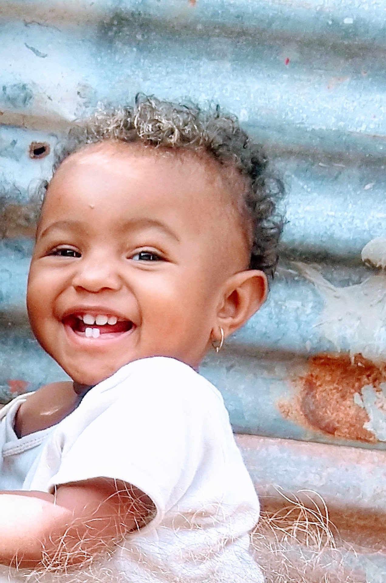 Maïssane participe au concours pour gagner de l'argent avec cette photo : toddler, child, smiling, happy, face, curly_hair, earring, white_shirt, portrait, closeup, skin, teeth, rusty_background, metal, outdoor, candid, cute, person, joy, expression