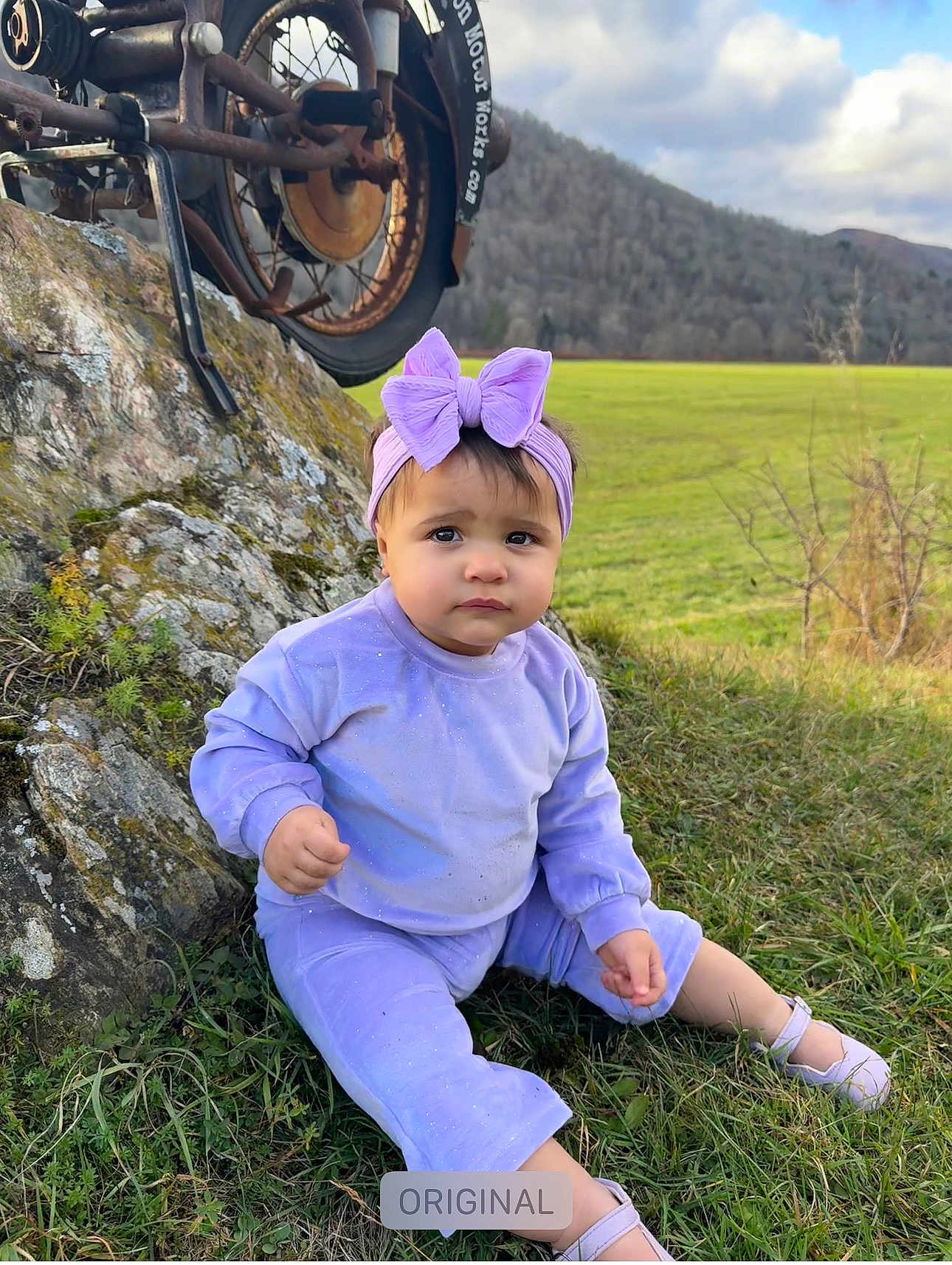 Kylie joined the competition — help win amazing prizes! toddler, child, outdoor, grass, rock, mountain, cloudy_sky, motorcycle_wheel, purple_clothing, headband, bow, sitting, nature, field, shoes, cute, portrait, casual, sparkle, scenic