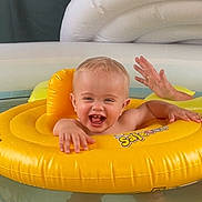 Fin is registered to the contest to win money with this photo: baby, child, pool, water, inflatable_ring, yellow, smile, happy, face, person, hand, teeth, floating, swimming, summer, fun, playful, indoor, light, toy