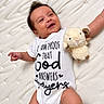 baby, infant, smiling, happy, portrait, lying_down, bed, quilt, white_bedding, plush_toy, lamb, stuffed_animal, onesie, clothing, arms, legs, dark_hair, indoor, close_up, nursery
