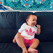 Zyaria joined the competition — help win amazing prizes! barefoot, casual, child, clothing, couch, cute, happy, home, indoor, laughing, patterned_wall_hanging, person, pink_shorts, portrait, sitting, smiling, tapestry, toddler, white_shirt, young_child