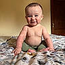 baby, child, smile, sitting, bed, bedspread, floral_pattern, indoor, room, wooden_door, wall, cute, cheeks, hands, feet, bare_chest, pants, portrait, infant, happy