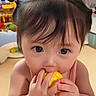 baby, child, curious_eyes, curly_hair, cute, eating, face, fruit, indoors, innocence, pigtails, pink_clothing, playroom, portrait, sitting, small_hands, toddler, toy, yellow, young_child