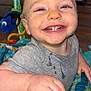 baby, smiling, teeth, face, hand, play_seat, toy, fish_toy, clothing, gray_shirt, indoor, happy, child, infant, person, mouth, expression, blue, orange, green