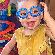 Tiago a rejoint le concours — aidez-le/la à gagner de superbes lots ! toddler, child, glasses, toy_glasses, yellow_shirt, winnie_the_pooh, smiling, happy, indoor, toys, plastic_toys, red_dragon, toy_track, playful, cute, buttoned_shirt, short_hair, face, hand, expression