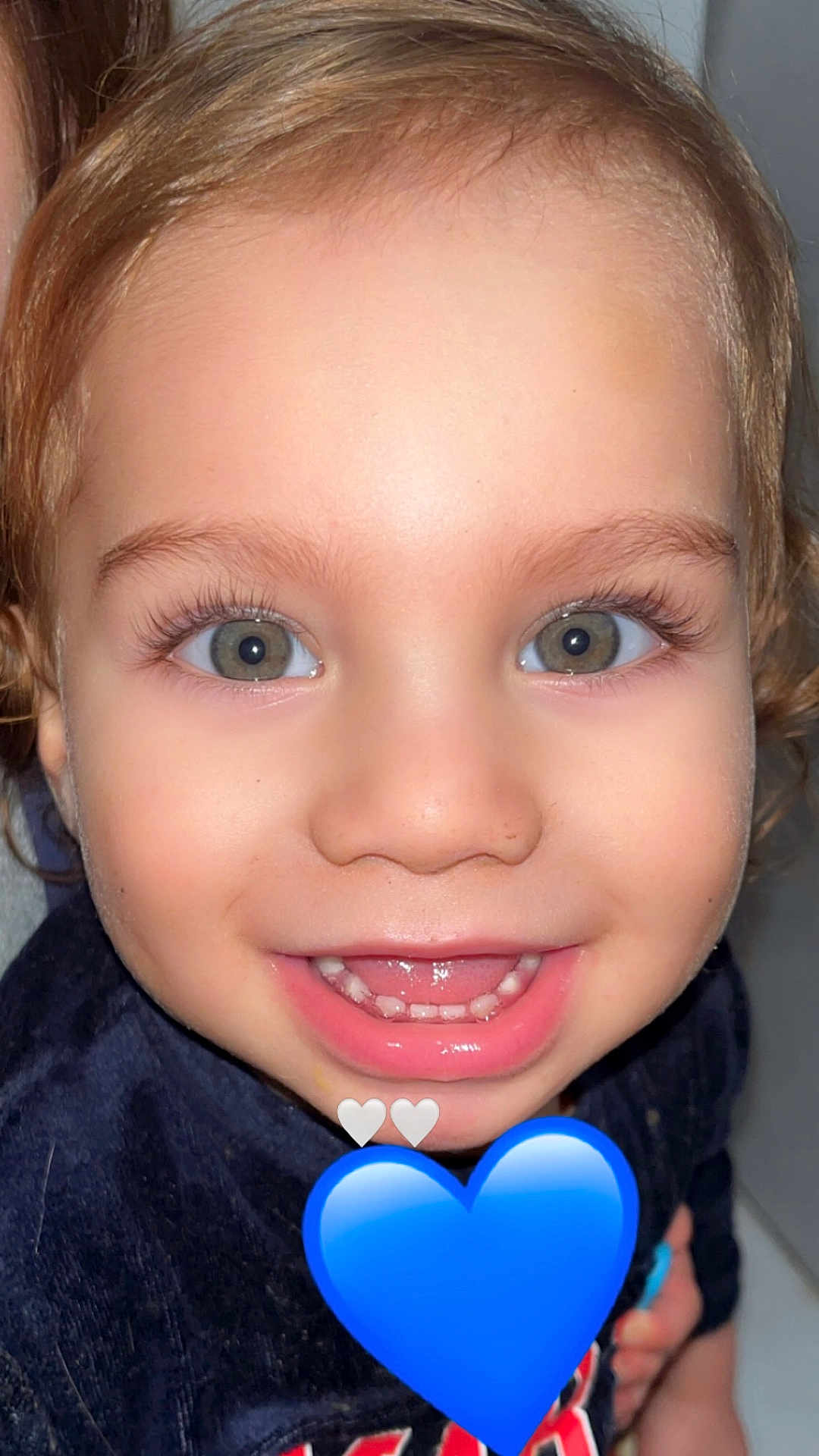 Tiago participe au concours pour gagner de l'argent avec cette photo : child, toddler, smiling, face, eyes, teeth, curly_hair, blue_heart_emoji, white_hearts, close_up, portrait, joyful, cute, young_child, happy, skin, clothing, indoor, person, expression