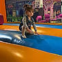 toddler, child, indoor, playground, inflatable, pigtails, overalls, striped_shirt, socks, colorful, chairs, mural, play_area, fun, balance, young_child, candid, portrait, floor, activity