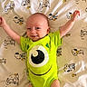baby, child, infant, smiling, happy, lying_down, arms_raised, green_onesie, monster_costume, cartoon, snoopy, blanket, bed, indoor, portrait, face, eyes, short_hair, cute, photography