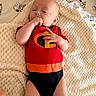 baby, infant, child, sleepy, lying_down, portrait, red_clothing, orange_clothing, black_clothing, onesie, blanket, knitted_blanket, bedding, snoopy, cartoon_pattern, cozy, indoors, bed, hand_in_mouth, baby_photography