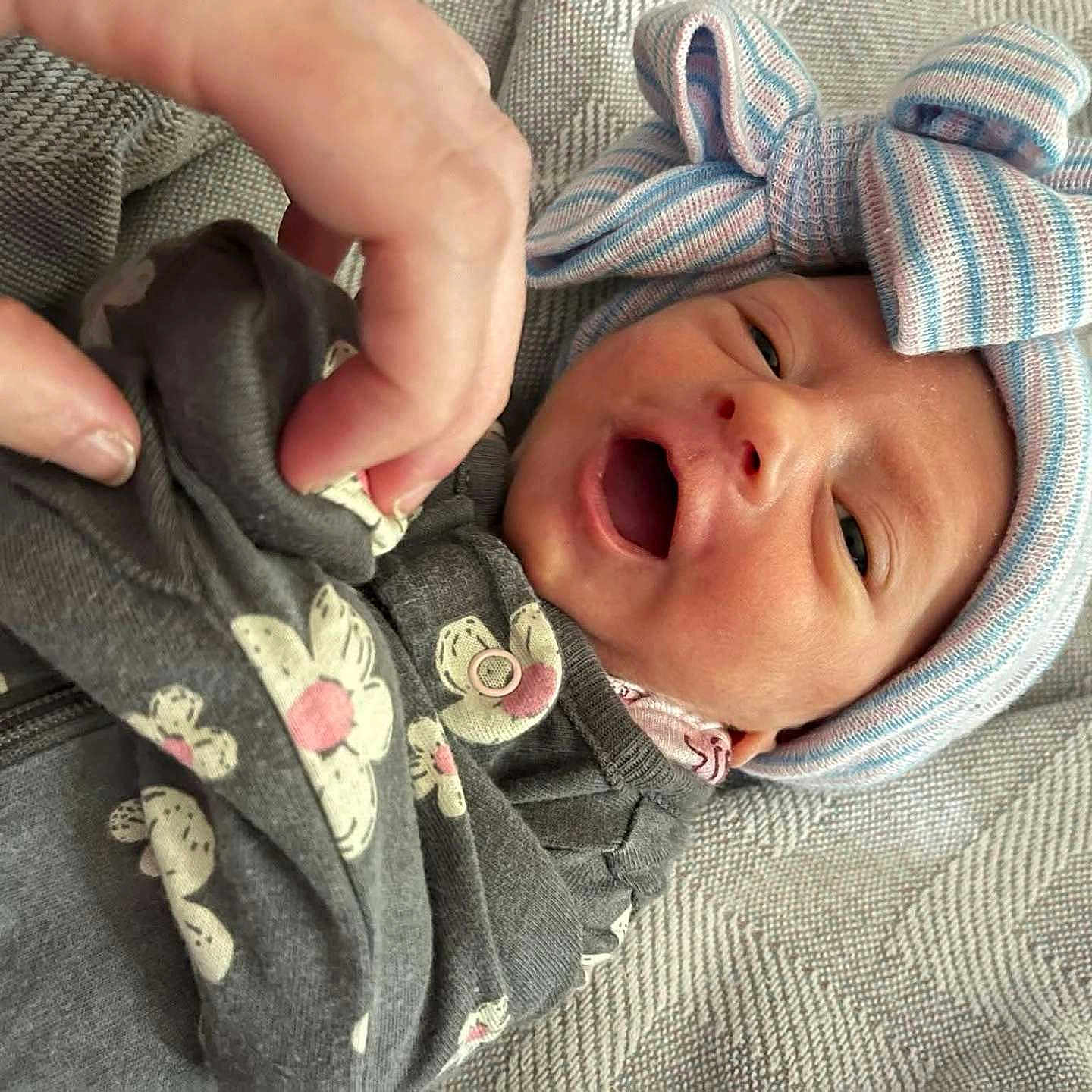 Theda is registered to the contest to win money with this photo: baby, blanket, bow, closeup, clothing, comfort, cute, fabric, face, floral_pattern, hand, hat, indoors, infant, newborn, person, portrait, skin, smile, soft