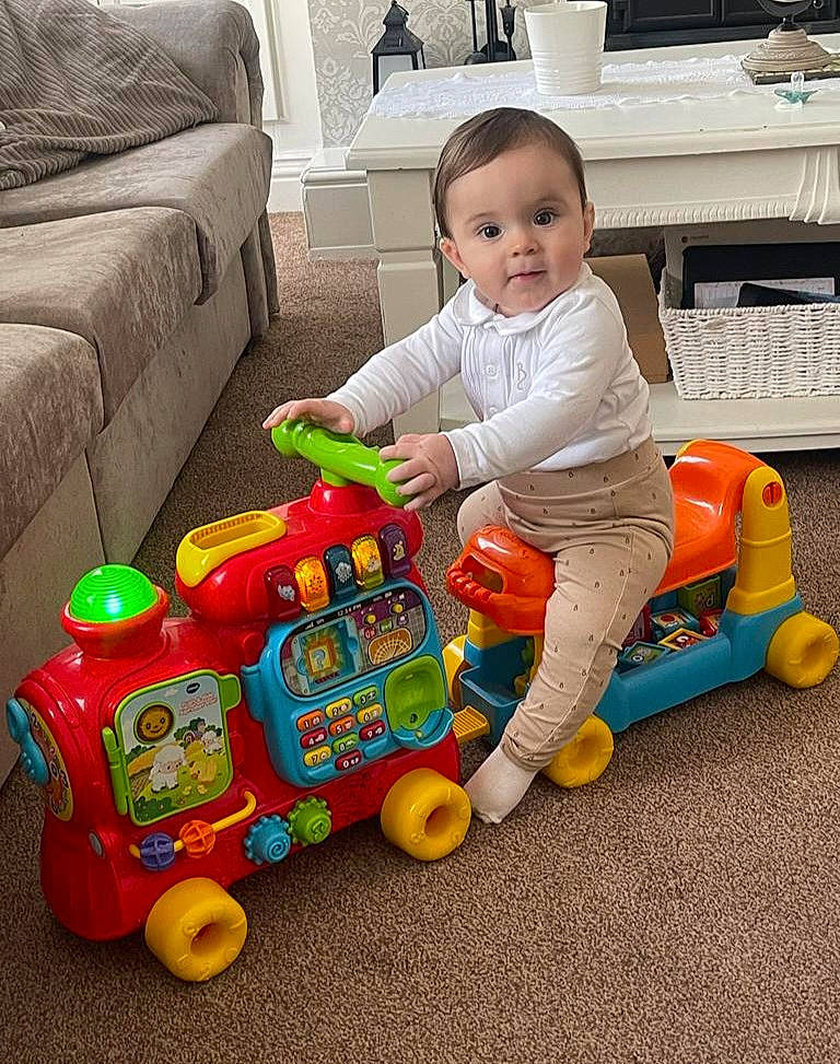 Charlie is registered to the contest to win money with this photo: baby, baby_playing_with_toys, baby_toddler_clothing, child, comfort, computer_keyboard, couch, fun, happy, peripheral, person, play, product, riding_toy, sharing, tire, toddler, toy, toy_vehicle, vehicle