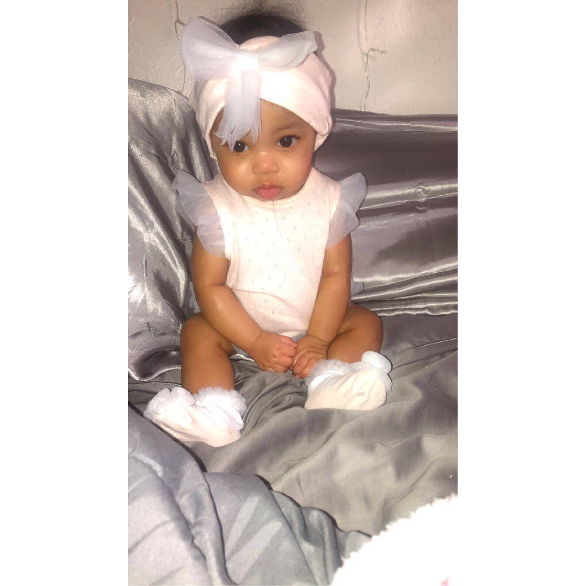 Alaia is registered to the contest to win money with this photo: arm, baby, baby_toddler_clothing, bedding, child, comfort, costume_hat, eyelash, fashion_accessory, formal_wear, hand, happy, headwear, human_body, human_leg, linens, neck, pattern, person, sitting
