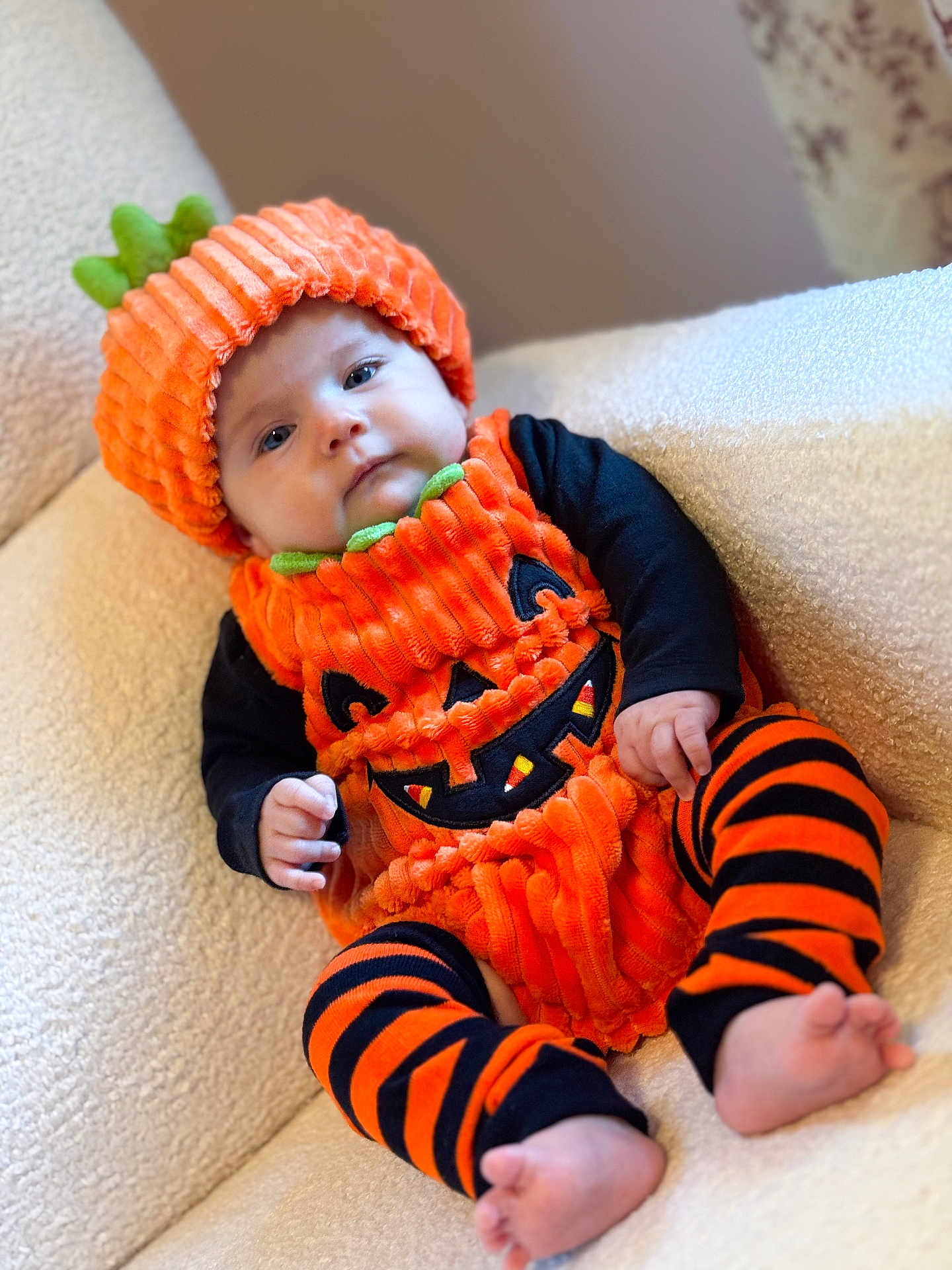 Ellie joined the competition — help win amazing prizes! baby, infant, pumpkin_costume, orange, black, striped_leggings, hat, cute, child, costume, halloween, chair, soft_furniture, indoors, portrait, face, feet, hands, cozy, expression