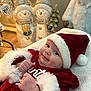 baby, smiling, santa_hat, christmas_outfit, holiday, festive, snowman_decoration, santa_figure, cozy, blanket, indoors, cute, child, portrait, holiday_decor, red_clothing, white_fur, holiday_spirit, festive_season, holiday_cheer