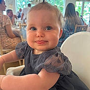 Harper is registered to the contest to win money with this photo: baby, child, tongue_out, high_chair, dress, ponytail, blue_eyes, indoor, people, blurred_background, table, chair, event, cute, smile, person, infant, celebration, face, fun