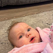 Harper is registered to the contest to win money with this photo: baby, blue_eyes, carpet, child, childhood, close_up, cozy, curious, cute, expression, face, indoor, infant, laying_down, newborn, person, pink_robe, skin, soft_texture, young