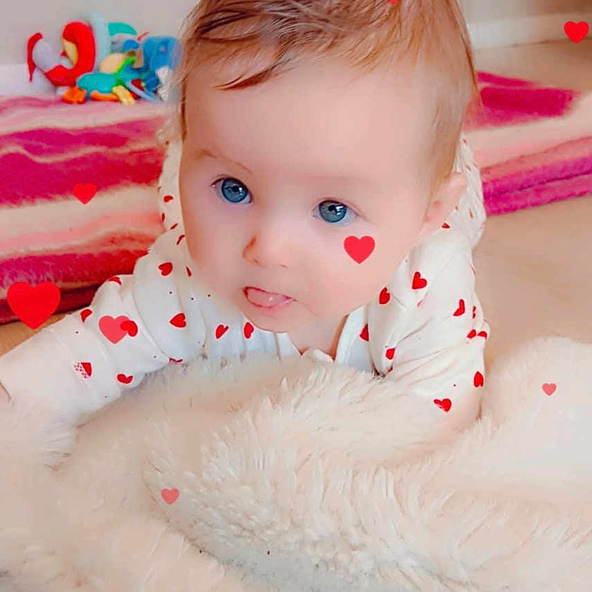 Shelsea a rejoint le concours — aidez-le/la à gagner de superbes lots ! baby, infant, face, blue_eyes, crawling, blanket, indoor, toy, heart_filter, pink_rug, floor, cute, child, person, soft_texture, white_blanket, playful, young_child, head, expression