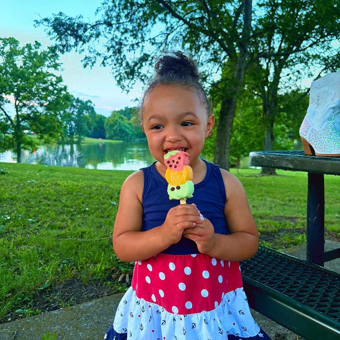 Adalyn is registered to the contest to win money with this photo: child, girl, ice_cream, dress, outdoor, park, grass, tree, lake, smile, summer, picnic_table, food, happy, nature, daylight, playful, cute, holding, casual