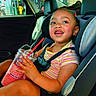 child, toddler, car_seat, car_interior, drink, slushie, pink_drink, red_straw, smiling, happy, seatbelt, striped_shirt, shorts, window, gas_station, daylight, skin, hands, face, hair