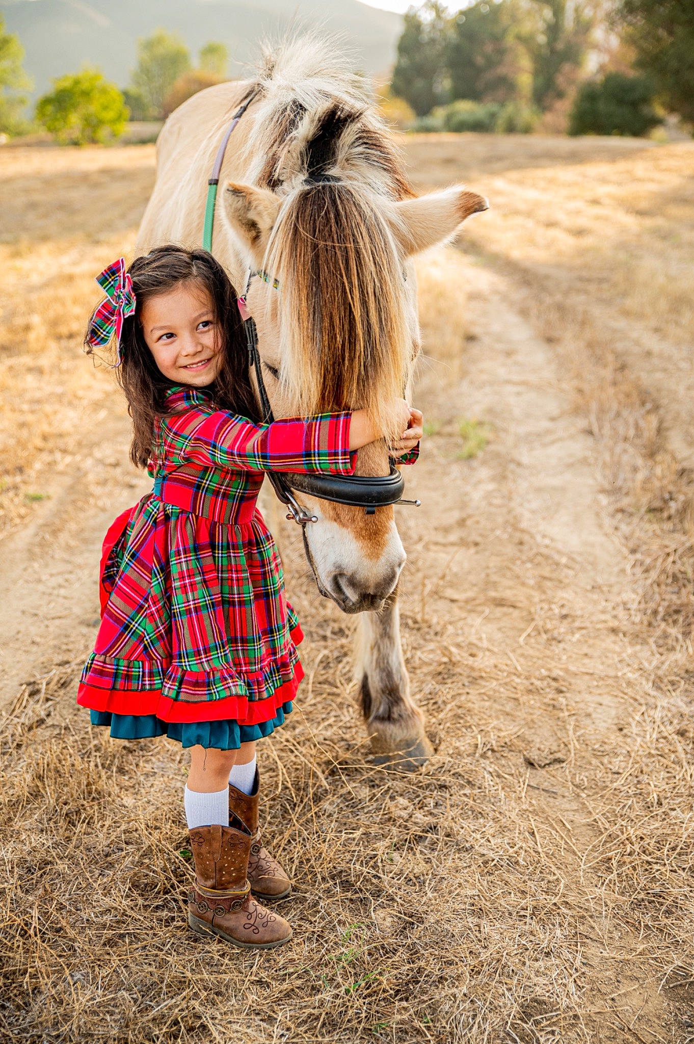 Brighton is registered to the contest to win money with this photo: dress, fawn, footwear, fun, grass, grassland, hair, happy, head, horse, joy, landscape, outerwear, people_in_nature, person, plaid, plant, shoe, tartan, toddler