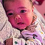 baby, infant, close_up, face, eyes, onesie, patterned_clothing, hand, pillow, sleeping_area, indoors, cute, child, young, skin, head, expression, person, resting, cozy