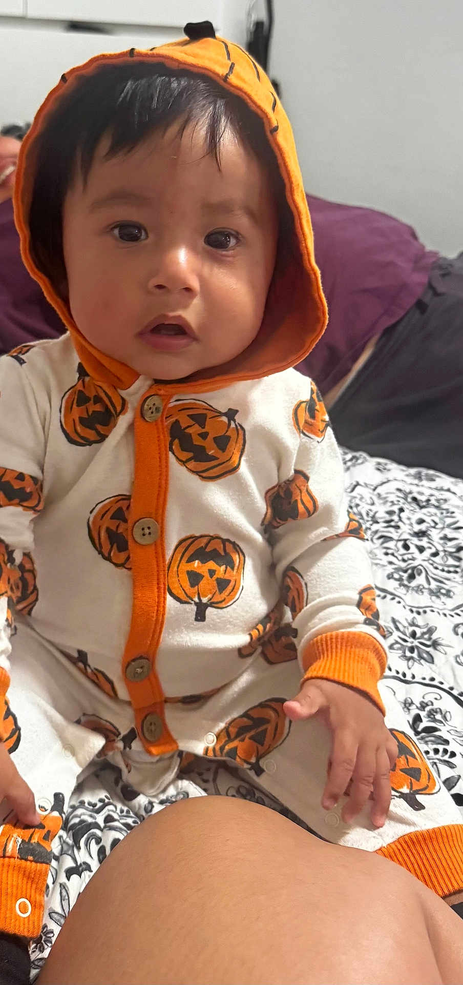 Ezekiel joined the competition — help win amazing prizes! baby, child, pumpkin, hoodie, onesie, orange, white, pattern, bedspread, hand, face, indoors, person, cute, expression, sitting, clothing, portrait, young_child, festive