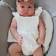 Freyja joined the competition — help win amazing prizes! baby, infant, child, white_dress, flower_headband, cushioned_seat, cute, chubby_cheeks, portrait, indoors, soft_lighting, newborn, baby_clothing, adorable, sitting, person, skin, head, hand, foot