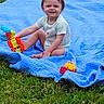 toddler, child, smile, blue_blanket, grass, outdoor, toy_truck, playing, happy, sitting, green, young_child, short_hair, casual_clothing, daylight, nature, fun, cute, person, baby