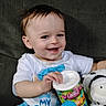 David is registered to the contest to win money with this photo: toddler, child, smiling, blue_pants, white_shirt, plush_toy, zebra_toy, container, fruit_chews, basket, indoor, couch, happy, face, hand, sitting, cute, young_child, playful, portrait
