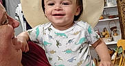 David is registered to the contest to win money with this photo: baby, child, adult, hat, cowboy_hat, dinosaur_print, onesie, smile, indoor, person, holding, happy, face, family, furniture, basket, painting, shelf, chair, home