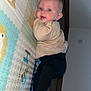baby, infant, play_mat, floor, indoor, child, cute, clothing, face, head, person, smile, wall, wooden_floor, furniture, socket, pants, sweater, curious, lying_down