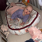 Mia participe au concours pour gagner de l'argent avec cette photo : baby, baby_bedding, baby_nest, bedroom, blanket, child, comfort, crib, cute, face, indoor, infant, plush_toy, purple_clothing, resting, sleeping_area, smiling, soft_toys, toddler, wooden_crib