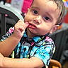 Josai is registered to the contest to win money with this photo: toddler, child, face, portrait, curious, expression, hand, lip, shirt, floral_pattern, colorful, indoors, chair, wood, person, cute, young_child, clothing, closeup, bright