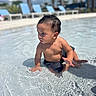 toddler, child, water, pool, summer, outdoor, sunlight, swimwear, sitting, curious, wet_hair, reflection, blue_chairs, palm_trees, sky, daytime, shallow_water, ripples, vacation, relaxation
