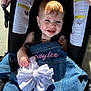 toddler, child, stroller, denim_jacket, bow, smiling, blue_eyes, sunlight, earring, clothing, baby, seatbelt, outdoor, portrait, cute, happy, face, person, holding, fabric