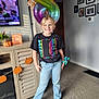 balloon, birthday, blonde_hair, cabinet, carpet, casual_clothing, child, decoration, family_photos, happy, indoor, jeans, living_room, number_8, pumpkin, smiling, sock, television, toy, tshirt