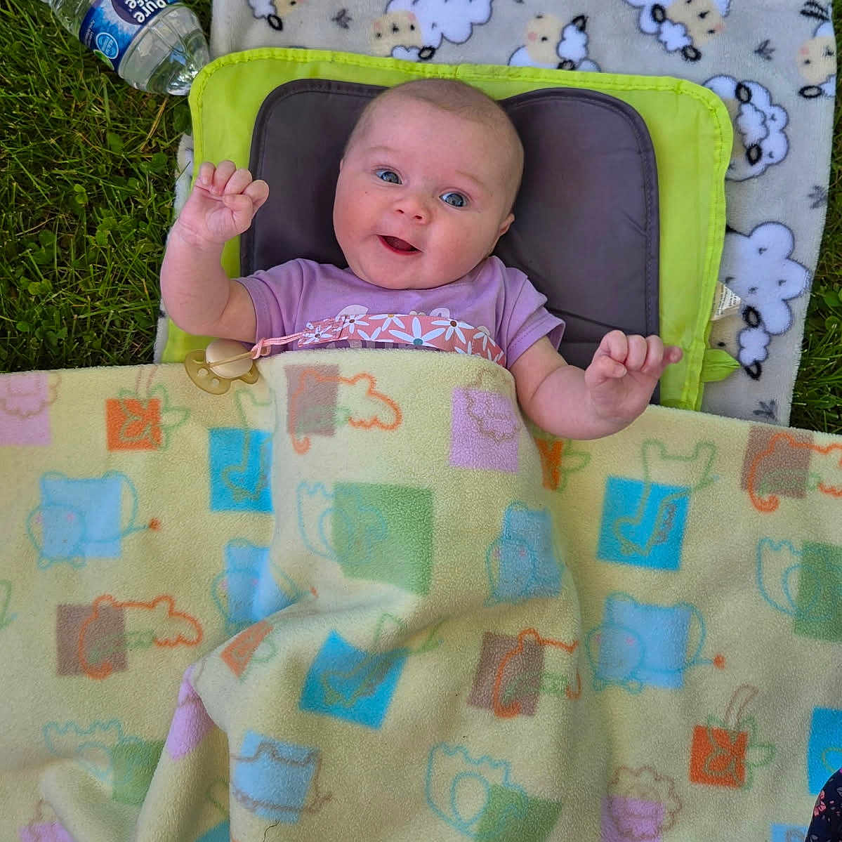 Dawna joined the competition — help win amazing prizes! baby, blanket, clothing, colorful, face, grass, hand, happy, head, lying_down, nature, outdoor, pacifier, person, playful, sheep_pattern, smiling, soft_texture, toddler, water_bottle