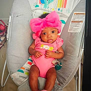 Royalty joined the competition — help win amazing prizes! baby, infant, child, portrait, sitting, bouncer, baby_seat, pink_outfit, hair_bow, headband, wide_eyes, neutral_expression, nursery, indoor, colorful_background, floral_clothing, baby_shoes, cushion, playful, photograph