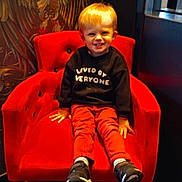 Noa a rejoint le concours — aidez-le/la à gagner de superbes lots ! black_sweater, casual_clothing, child, cute, decorative_wall, furniture, happy, home_interior, indoor, lighting, person, portrait, red_chair, red_pants, seated, smiling, sneakers, toddler, window, young_child