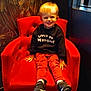 toddler, child, smiling, red_chair, black_sweater, red_pants, sneakers, indoor, portrait, happy, decorative_wall, window, lighting, furniture, person, cute, seated, young_child, casual_clothing, home_interior