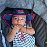 baby, child, infant, hat, blue_hat, american_flag, striped_clothing, onesie, sitting, fingers_in_mouth, stroller, canopy, red_trim, cute, portrait, young_child, summer, casual, comfortable, happy