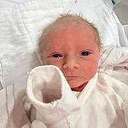 Jesse Jr is registered to the contest to win money with this photo: baby, newborn, infant, hospital, blanket, swaddle, onesie, mitten, face, eyes, gaze, closeup, portrait, skin, hair, hospital_bed, pillow, soft_lighting, white, peaceful_expression