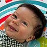 baby, child, smiling, tongue_out, face, eyes, hair, cheeks, clothing, patterned_shirt, play_mat, colorful, orange, blue, green, white, closeup, portrait, happy, infant