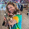 casual, clothing_rack, colorful, curly_hair, dog, friendly, happy, indoor, leash, pet, portrait, shelf, shopping, smile, social_media, store, tattoos, tie_dye_shirt, woman, wood_floor