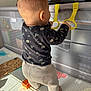 baby, baby_clothes, back_view, child, childhood, floor_mat, home, indoor, infant, padded_floor, plastic_rings, play_area, playpen, puzzle, standing, sunlight, toddler, toys, yellow_rings, young_child