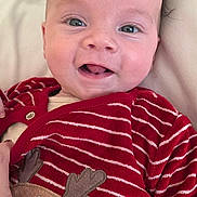 Jake is registered to the contest to win money with this photo: baby, infant, smile, face, red_clothing, striped, reindeer_applique, cute, happy, lying_down, soft_surface, closeup, child, newborn, expression, eyes, mouth, skin, hand, cozy