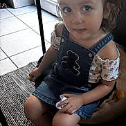 Sophie participe au concours pour gagner de l'argent avec cette photo : toddler, child, girl, indoor, denim_dress, pacifier, hair_clip, ponytail, footwear, sandals, floor_tiles, cushion, carpet, seated, curious, looking_up, short_sleeves, patterned_clothing, hand_holding_object, young_child