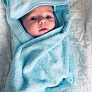 Lyam participe au concours pour gagner de l'argent avec cette photo : baby, blue_towel, blanket, face, hood, infant, lying_down, person, portrait, quilt, soft, snug, towel, wrapped, cute, child, cozy, baby_face, fabric, bed