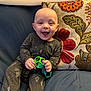 Miles is registered to the contest to win money with this photo: baby, child, smiling, toy, green_toy, onesie, space_theme, couch, pillow, floral_pillow, indoor, happy, sitting, cute, infant, clothing, face, hands, play, comfort