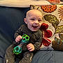 baby, smiling, toy, onesie, couch, pillow, blanket, indoor, child, happy, home, sitting, face, person, clothing, furniture, play, infant, cute, joyful
